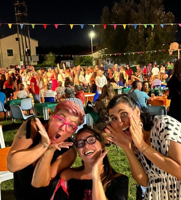 Strada festosa con bandiere e decorazioni colorate anni '80, persone in abbigliamento retrò che ballano, palco con musicisti in stile vintage, immagine di approfondimento